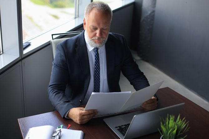 serious-mature-business-man-formalwear-reading-contract-while-sitting-desk-office.jpg